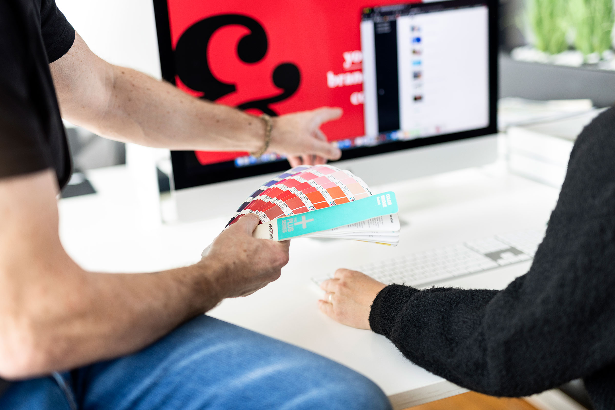 Zwei Angestellte von uspect beraten sich am Computer und stimmen Farben mit einem Farbfächer ab