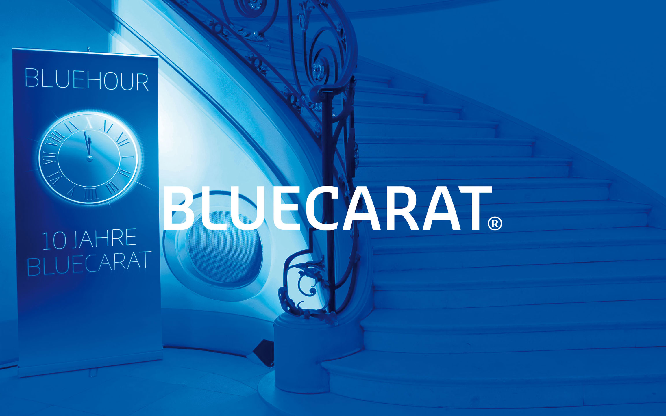 Bluecarat Logo vor blauem Hintergrund mit Rollup und Treppe auf einer Veranstaltung